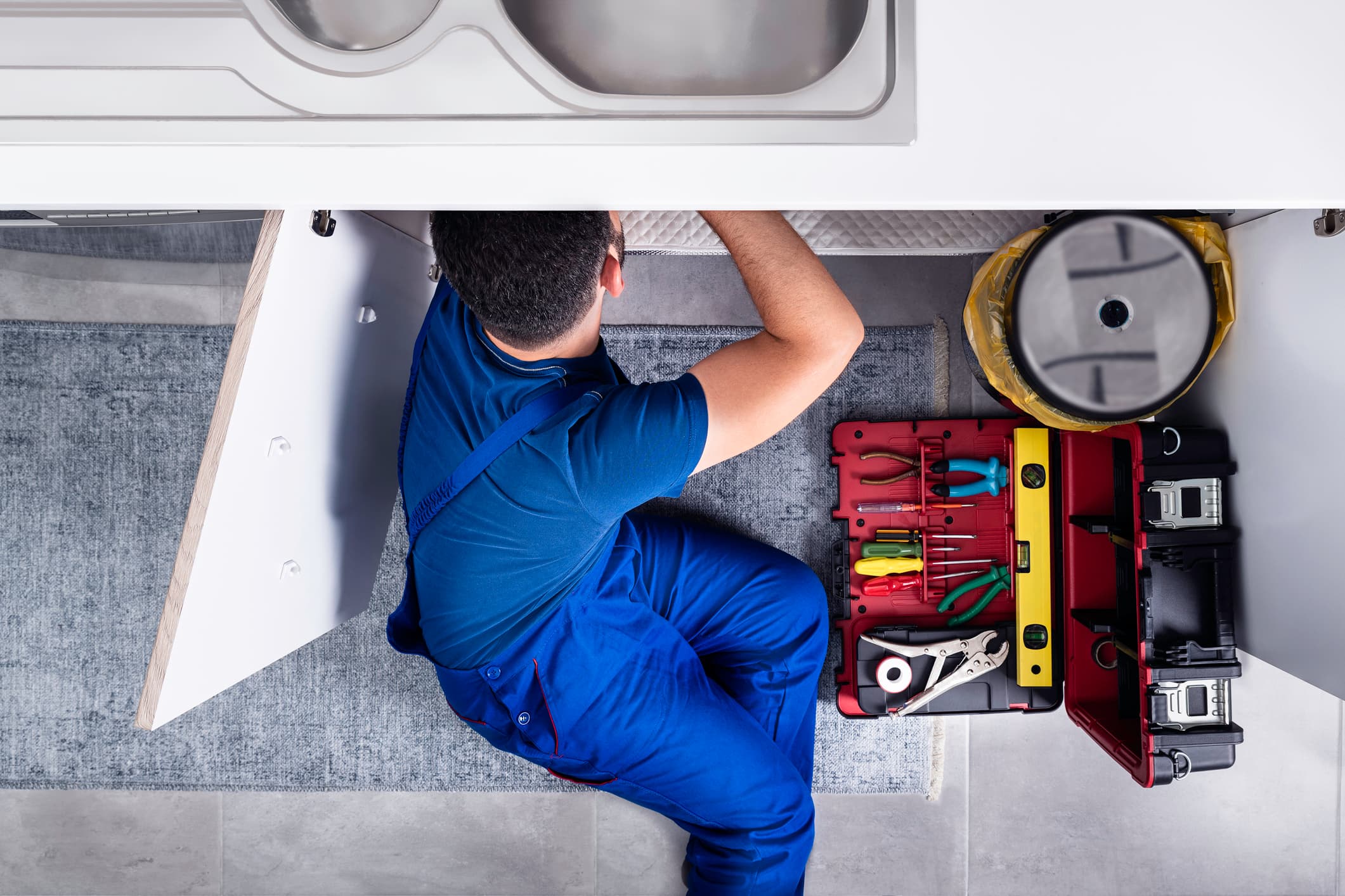 A plumber repairs a pipe beneath a sink