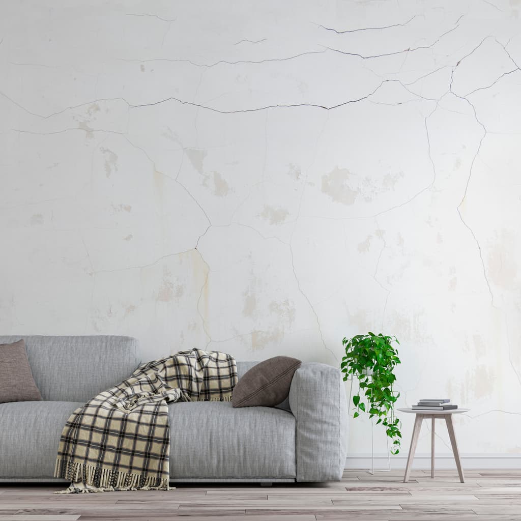 An apartment wall with cracks above a sofa.
