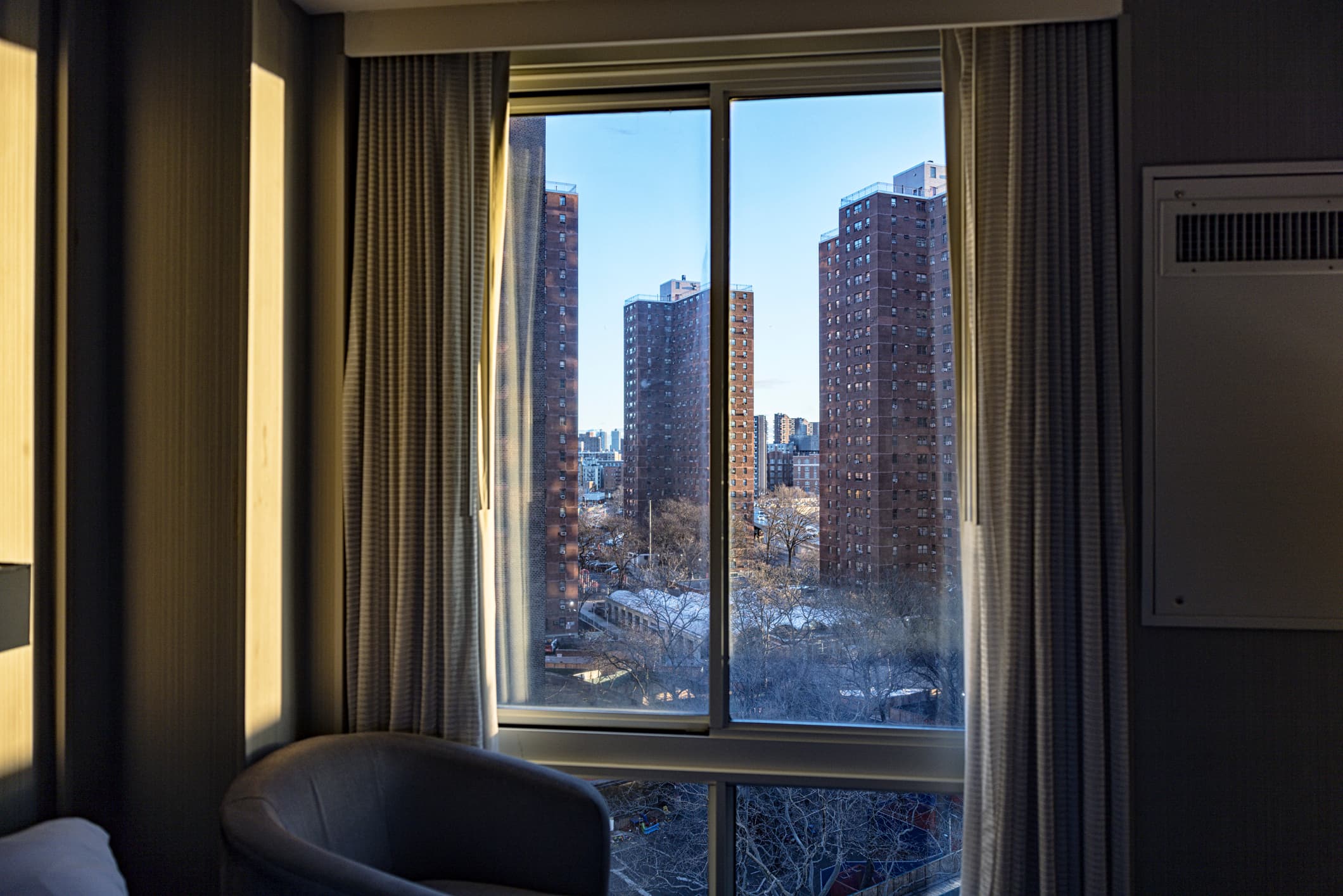 Several skyscraper city apartment buildings viewed through a generic upper east side Manhattan, New York City hotel bedroom window just after dawn sunrise.