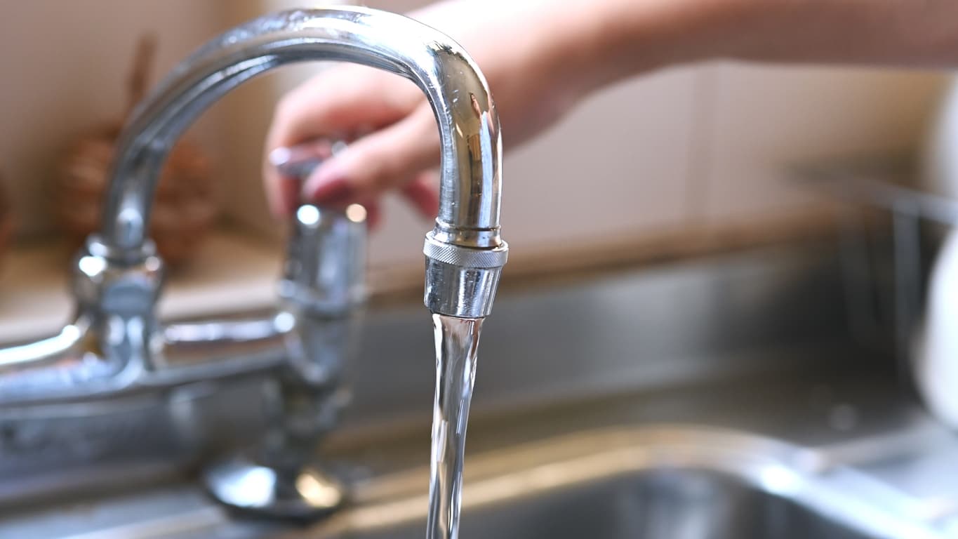 faucet with hand of woman in kitchen for cleaning, drinking and washing dishes. Interior, steel and household plumbing with sink and tap at home for stream, flowing and splash