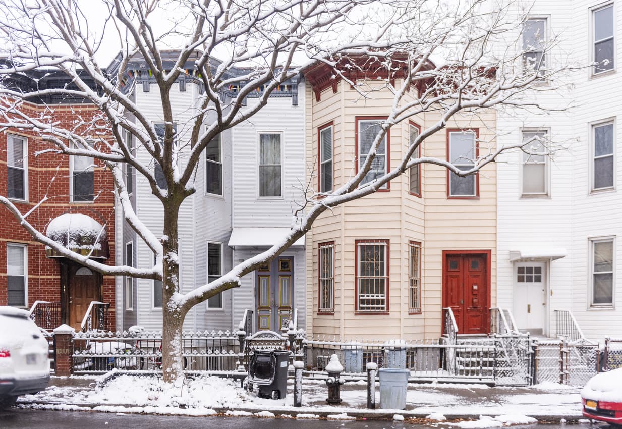 This is a front view of several residential buildings side by side along a street with snow on a winter day in Brooklyn, New York.